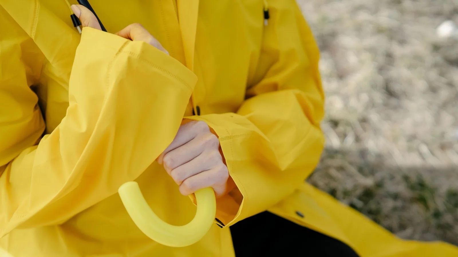 A detailed shot of a woman in a yellow raincoat holding an umbrella outdoors.