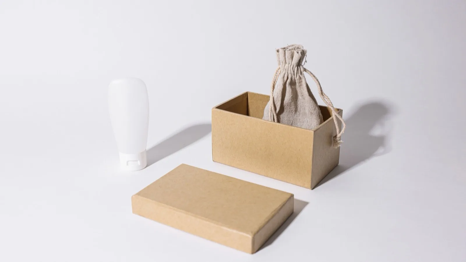 Stylish minimalist mockup featuring a cardboard box, linen pouch, and cream tube on a white background.