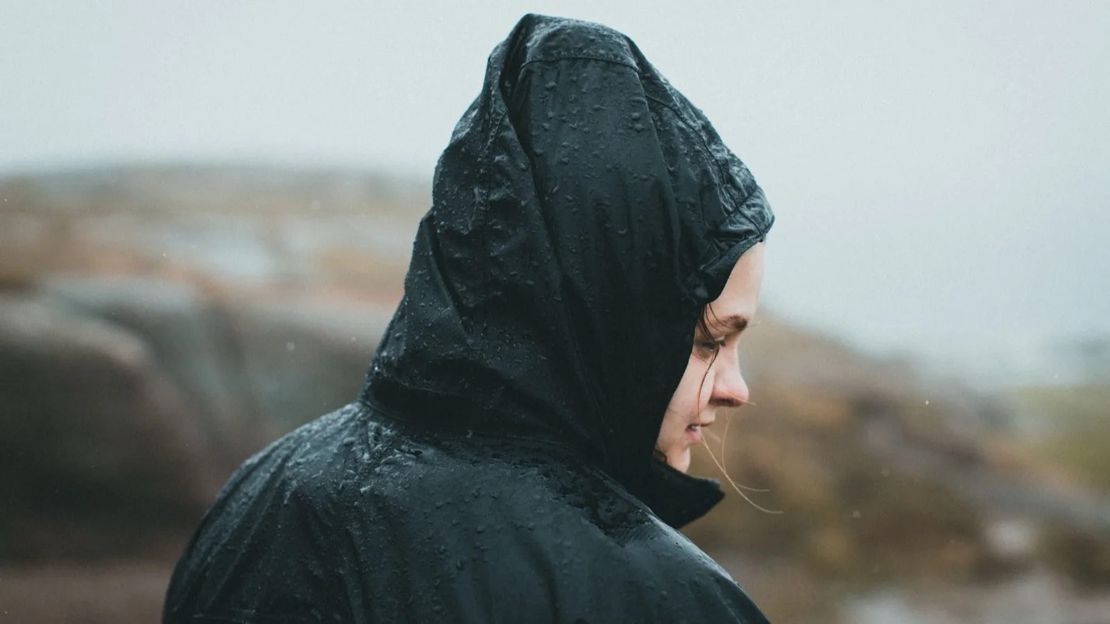 Side view of a woman in a rain jacket outdoors, experiencing rain with serene expression.